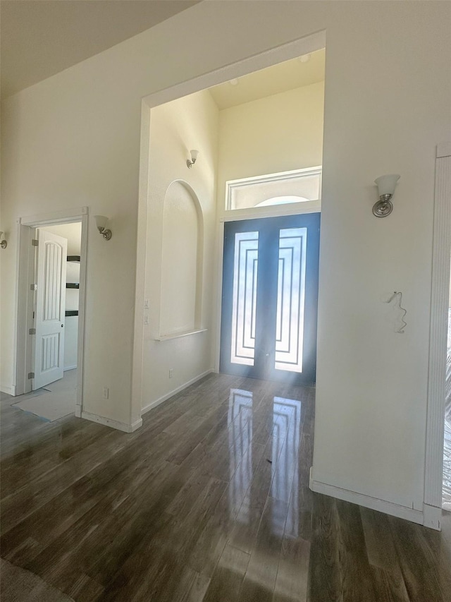foyer entrance with baseboards, wood finished floors, and a high ceiling