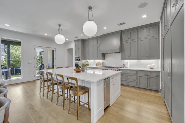 kitchen with backsplash, light wood-style flooring, custom range hood, and gray cabinets