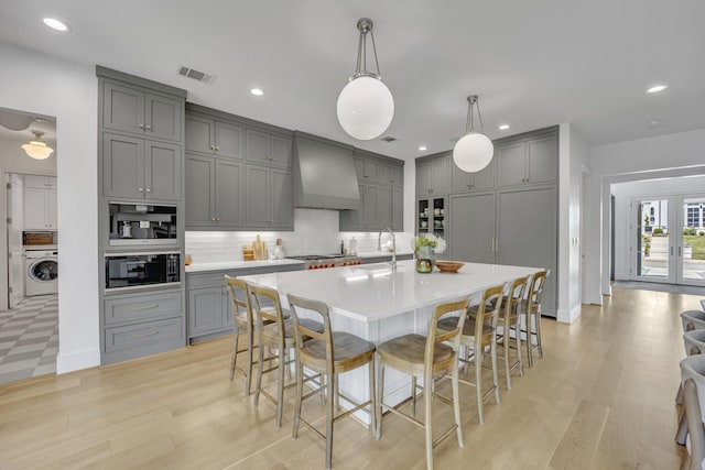 kitchen featuring tasteful backsplash, washer / clothes dryer, gray cabinetry, light countertops, and custom exhaust hood
