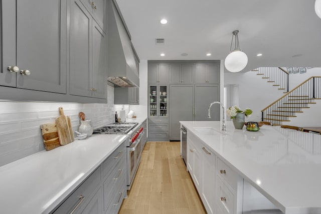7141 Lyre Ln, Dallas, TX 75214 - kitchen featuring a sink, gray cabinets, appliances with stainless steel finishes, wall chimney range hood, and light wood-style floors