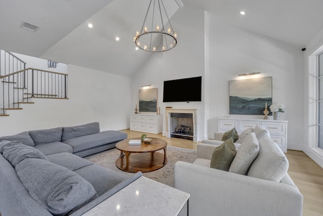 living area with light wood-style flooring, visible vents, high vaulted ceiling, a notable chandelier, and stairs