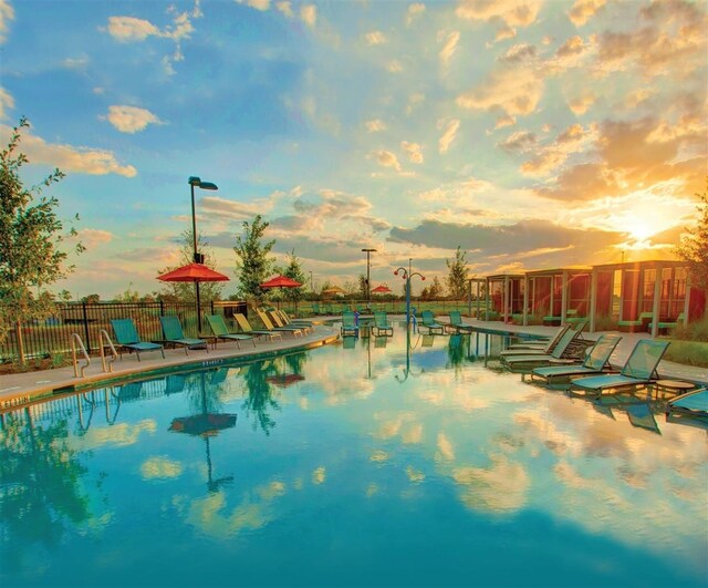 pool at dusk with fence, a patio area, and a community pool