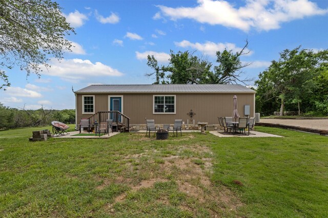 back of property featuring a lawn, a fire pit, metal roof, and a patio area