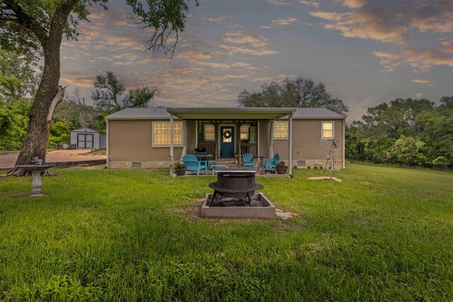 rear view of house featuring a storage unit, crawl space, metal roof, an outdoor fire pit, and a yard