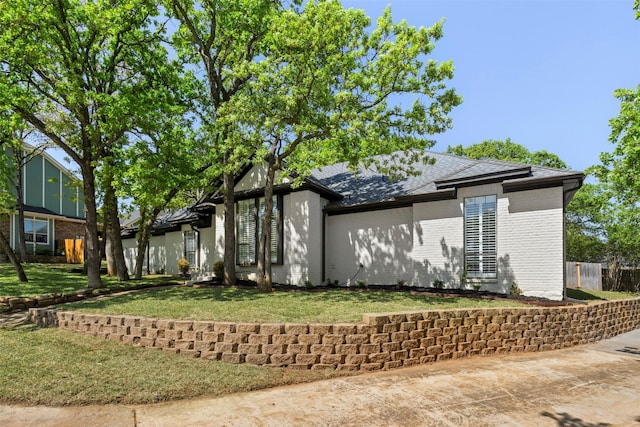 view of home's exterior featuring fence, a yard, a shingled roof, and brick siding