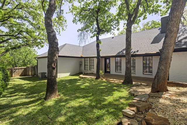back of house featuring brick siding, fence, a shingled roof, central AC, and a lawn