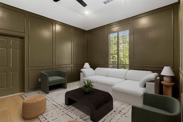living room featuring a decorative wall, a ceiling fan, and light wood finished floors