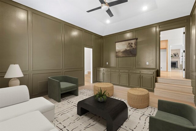 living area featuring visible vents, a decorative wall, a ceiling fan, and light wood finished floors