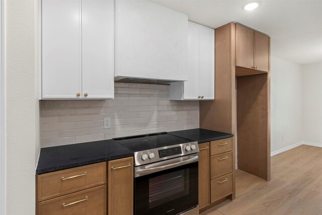 kitchen with light wood-style floors, stainless steel range with electric cooktop, backsplash, dark countertops, and white cabinets