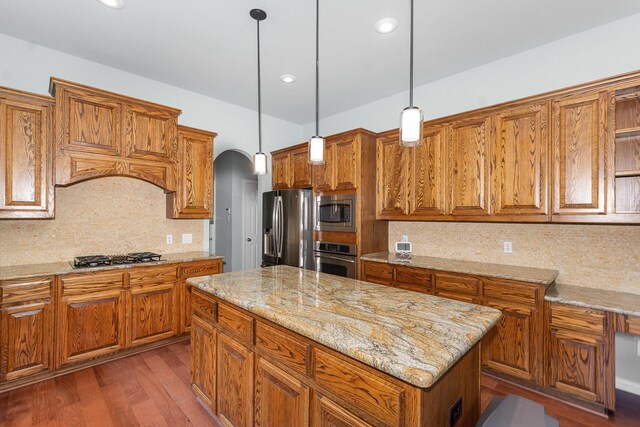 905 Maybach Ct, Mckinney, TX 75071 - kitchen featuring light stone counters, arched walkways, brown cabinetry, stainless steel appliances, and pendant lighting