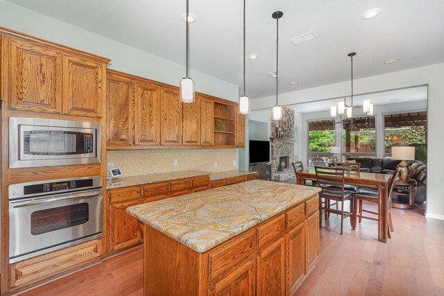 905 Maybach Ct, Mckinney, TX 75071 - kitchen featuring appliances with stainless steel finishes, light stone counters, light wood-style floors, brown cabinetry, and open floor plan