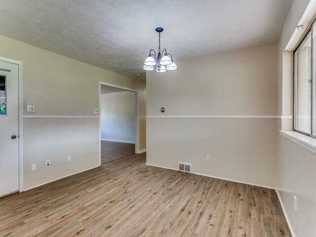 empty room with wood finished floors, baseboards, visible vents, a notable chandelier, and a textured ceiling