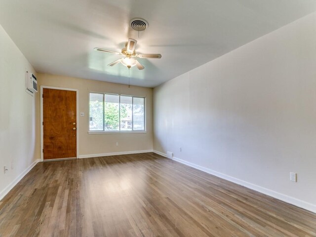 spare room featuring a wall mounted air conditioner, wood finished floors, a ceiling fan, and baseboards