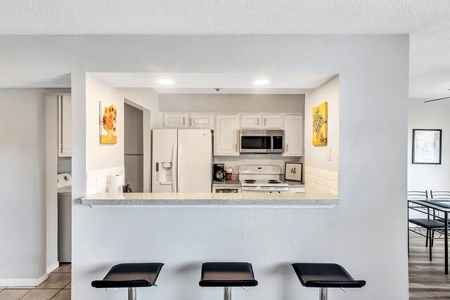 kitchen with a breakfast bar area, tasteful backsplash, white cabinets, light countertops, and white appliances
