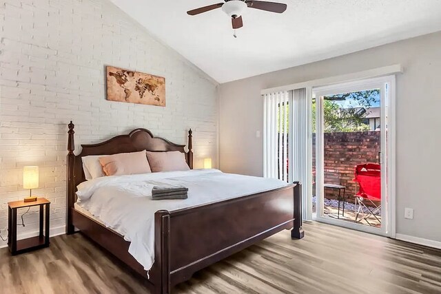 bedroom featuring lofted ceiling, wood finished floors, brick wall, and access to exterior