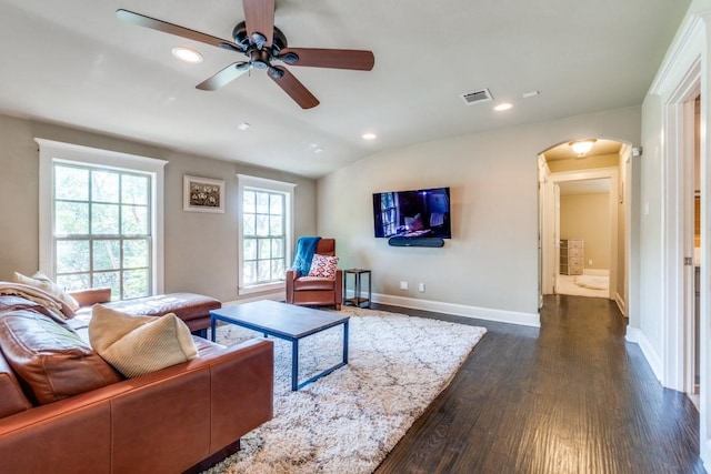 living room with dark wood-style floors, ceiling fan, visible vents, baseboards, and arched walkways