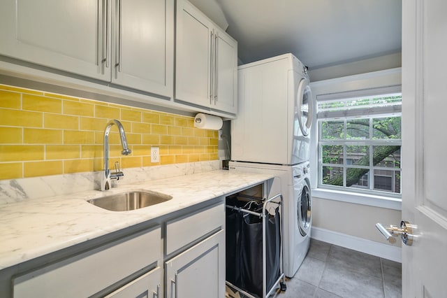 kitchen with tasteful backsplash, a sink, stacked washer / drying machine, baseboards, and tile patterned flooring