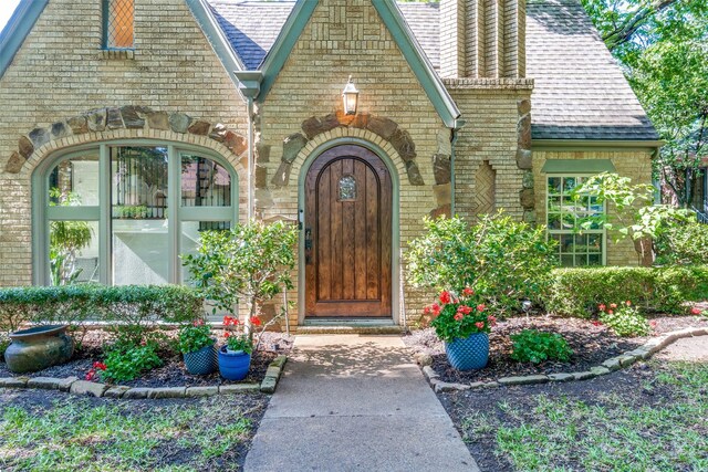 property entrance featuring a chimney, brick siding, and roof with shingles