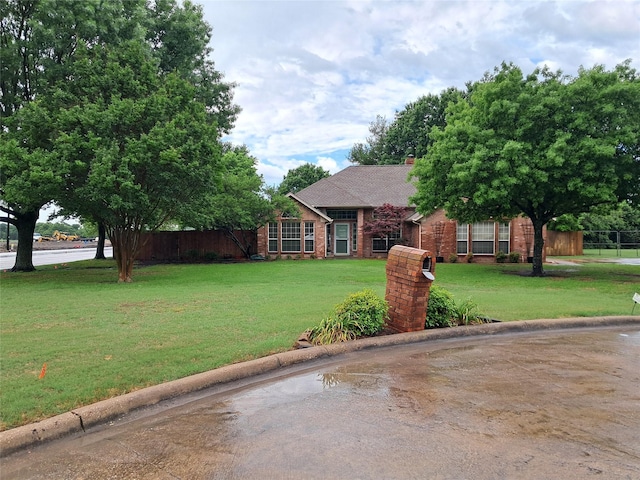 ranch-style house with fence, a chimney, a front yard, and brick siding