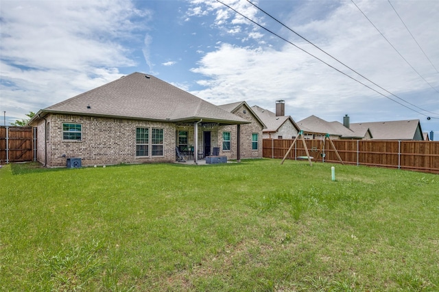 rear view of property featuring a fenced backyard, brick siding, roof with shingles, a playground, and a lawn