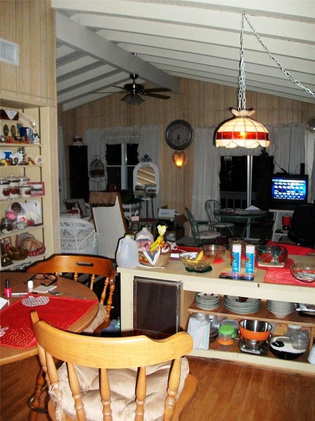 dining space featuring lofted ceiling with beams, a ceiling fan, visible vents, wood walls, and wood finished floors