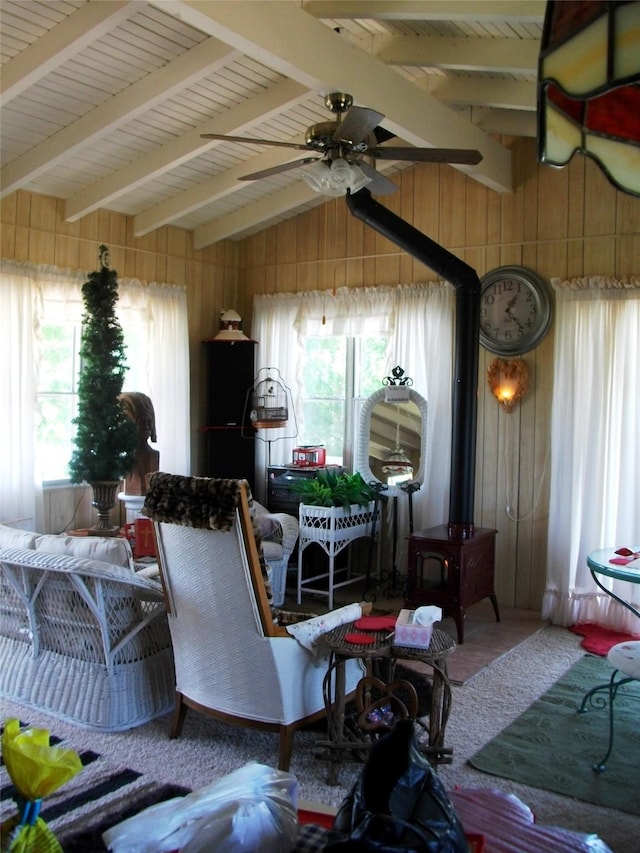 living room with lofted ceiling with beams, a wood stove, ceiling fan, and wood walls