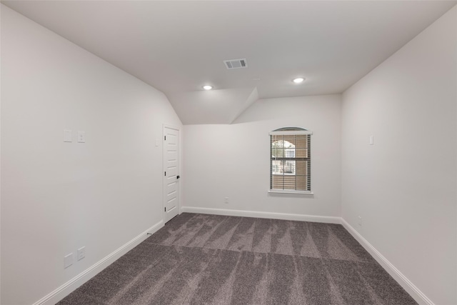 empty room featuring lofted ceiling, dark carpet, visible vents, baseboards, and recessed lighting
