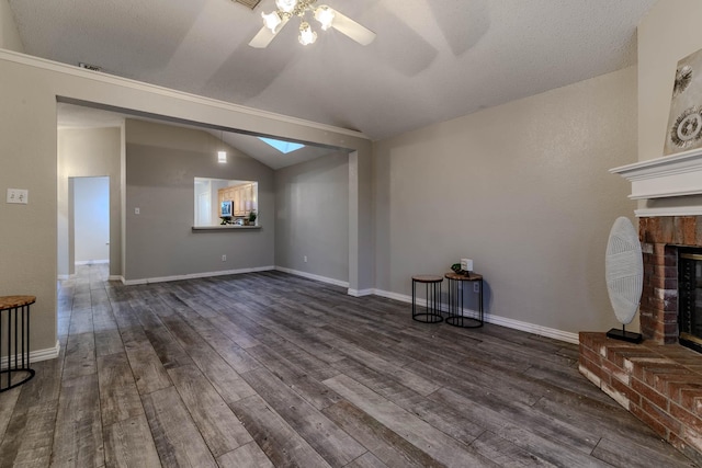 unfurnished living room featuring vaulted ceiling with skylight, a fireplace, baseboards, a ceiling fan, and dark wood-type flooring