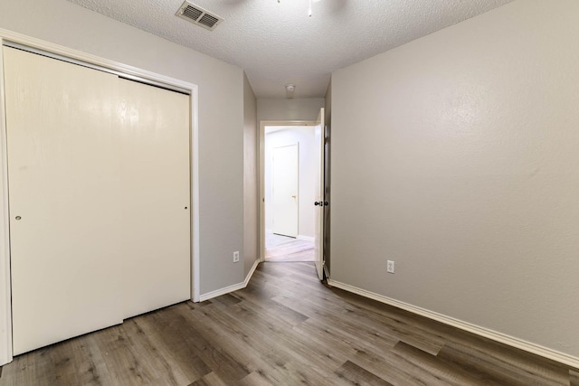 unfurnished bedroom with a textured ceiling, wood finished floors, visible vents, and a closet