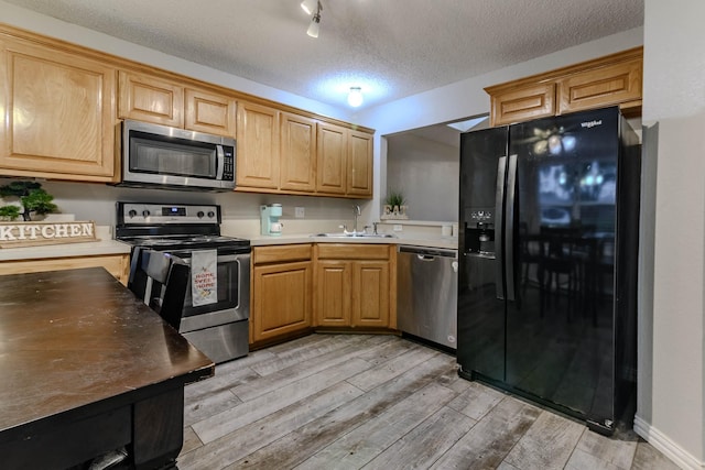 kitchen featuring a textured ceiling, a sink, appliances with stainless steel finishes, light countertops, and light wood finished floors