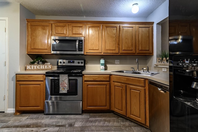 kitchen with brown cabinets, a sink, dark wood-type flooring, light countertops, and appliances with stainless steel finishes