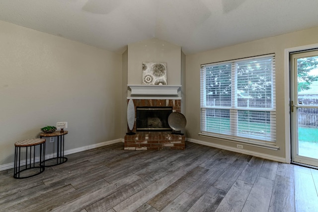 unfurnished room with lofted ceiling, wood finished floors, baseboards, and a brick fireplace