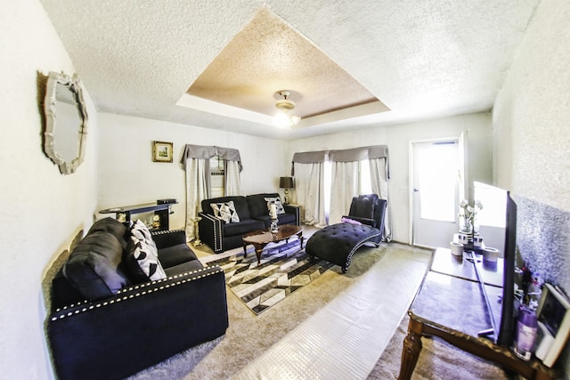 living area with a textured ceiling, carpet flooring, and a tray ceiling