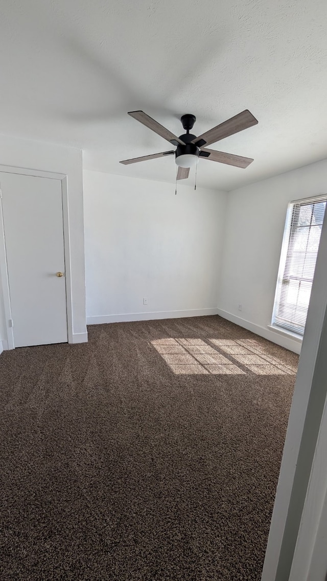 unfurnished room featuring baseboards, dark colored carpet, and ceiling fan