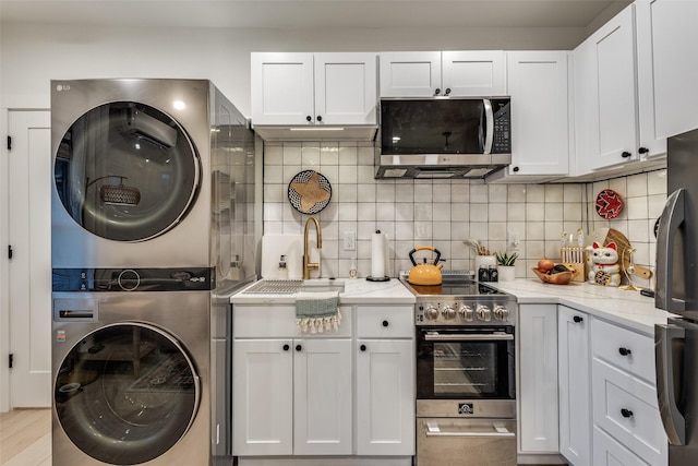 kitchen with light stone counters, decorative backsplash, stacked washer / dryer, stainless steel appliances, and white cabinets