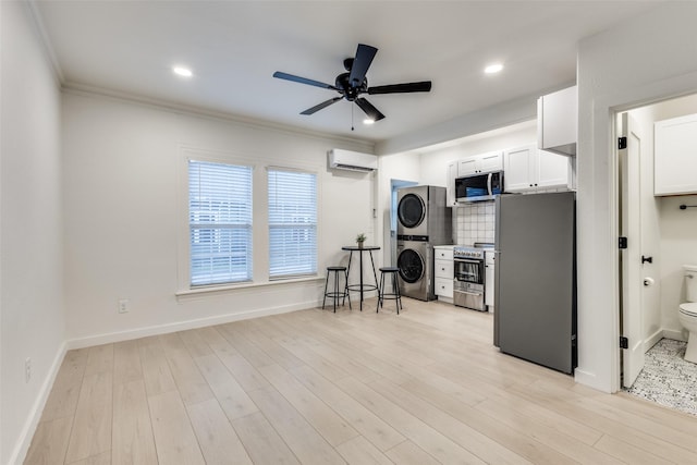 interior space with stacked washer and dryer, a wall unit AC, light wood finished floors, and a ceiling fan