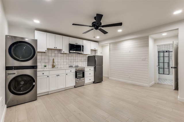 kitchen featuring a sink, ceiling fan, stacked washer and clothes dryer, light countertops, and appliances with stainless steel finishes