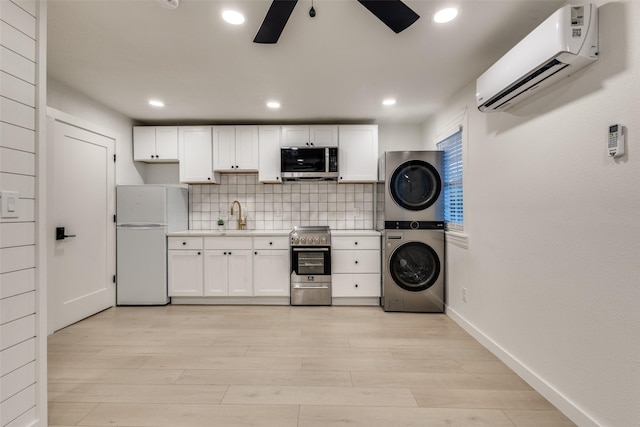 kitchen with appliances with stainless steel finishes, stacked washer and clothes dryer, light countertops, an AC wall unit, and a ceiling fan