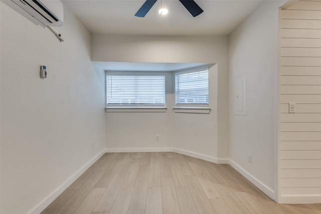 empty room with light wood-type flooring, a wall mounted air conditioner, ceiling fan, and baseboards