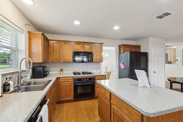 kitchen with light wood-style floors, a sink, backsplash, and black appliances