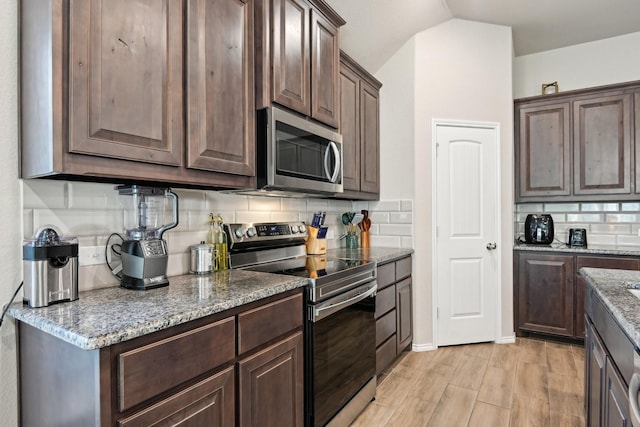 kitchen featuring tasteful backsplash, appliances with stainless steel finishes, dark brown cabinets, light stone countertops, and light wood finished floors
