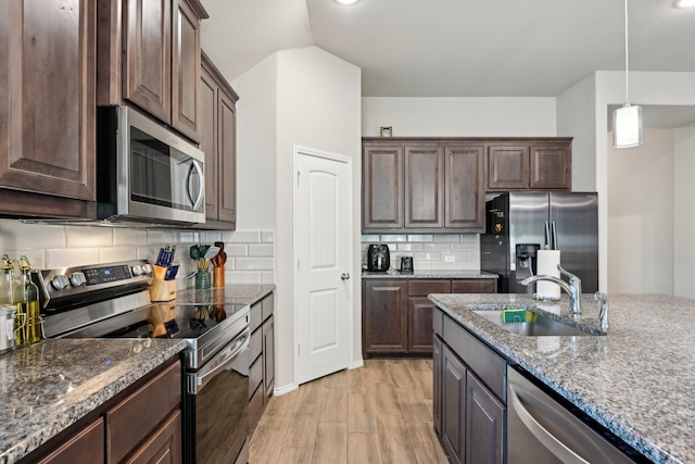 kitchen with stone countertops, stainless steel appliances, dark brown cabinets, and a sink
