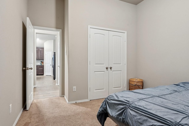 bedroom featuring a closet, freestanding refrigerator, light carpet, and baseboards