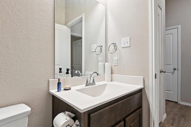 half bathroom featuring wood finished floors, a textured wall, toilet, and vanity