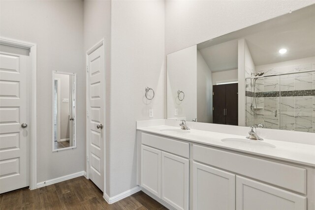full bath with double vanity, wood finished floors, a tile shower, and a sink
