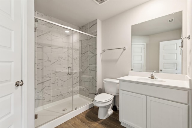 bathroom featuring wood finished floors, toilet, vanity, visible vents, and a marble finish shower