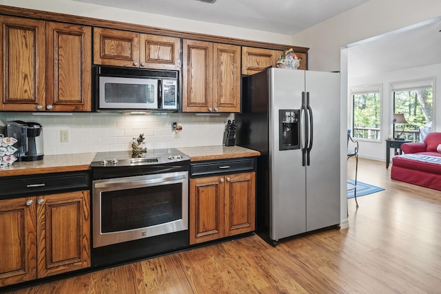 kitchen featuring light wood finished floors, stainless steel appliances, brown cabinetry, tasteful backsplash, and light countertops