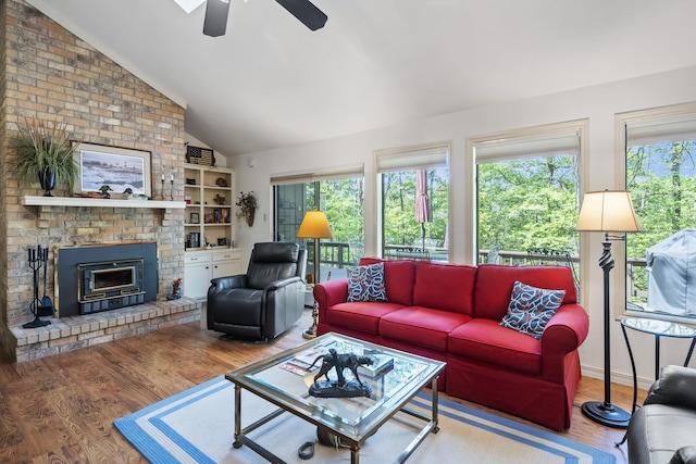 living area with wood finished floors, ceiling fan, a brick fireplace, and vaulted ceiling