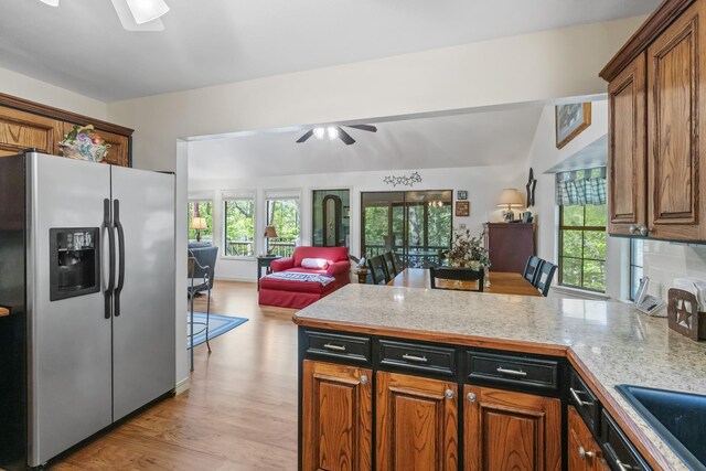 kitchen with light countertops, ceiling fan, stainless steel refrigerator with ice dispenser, a peninsula, and open floor plan