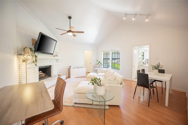 living room with crown molding, ceiling fan, a brick fireplace, wood finished floors, and high vaulted ceiling